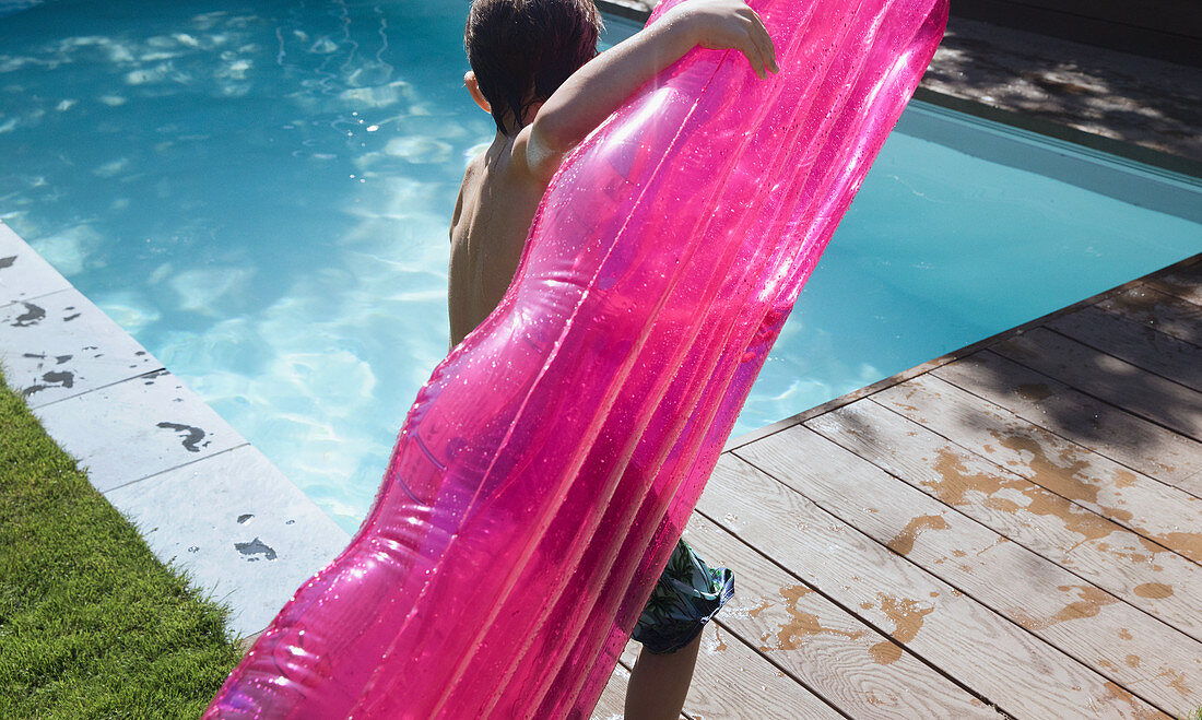 Boy with pink inflatable raft at summer poolside