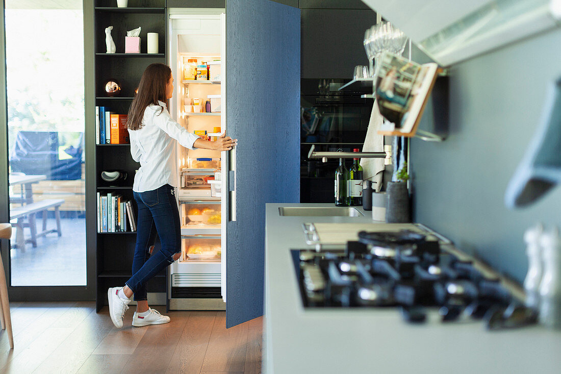 Woman standing at open refrigerator in kitchen