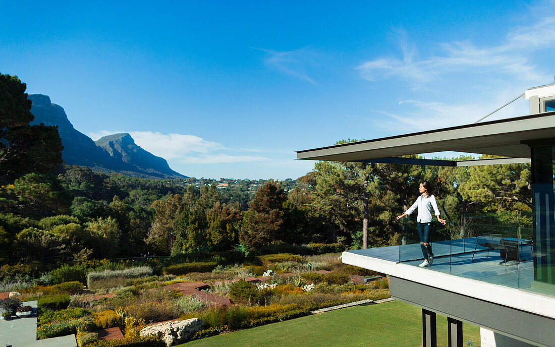 Woman standing on balcony overlooking garden and mountains
