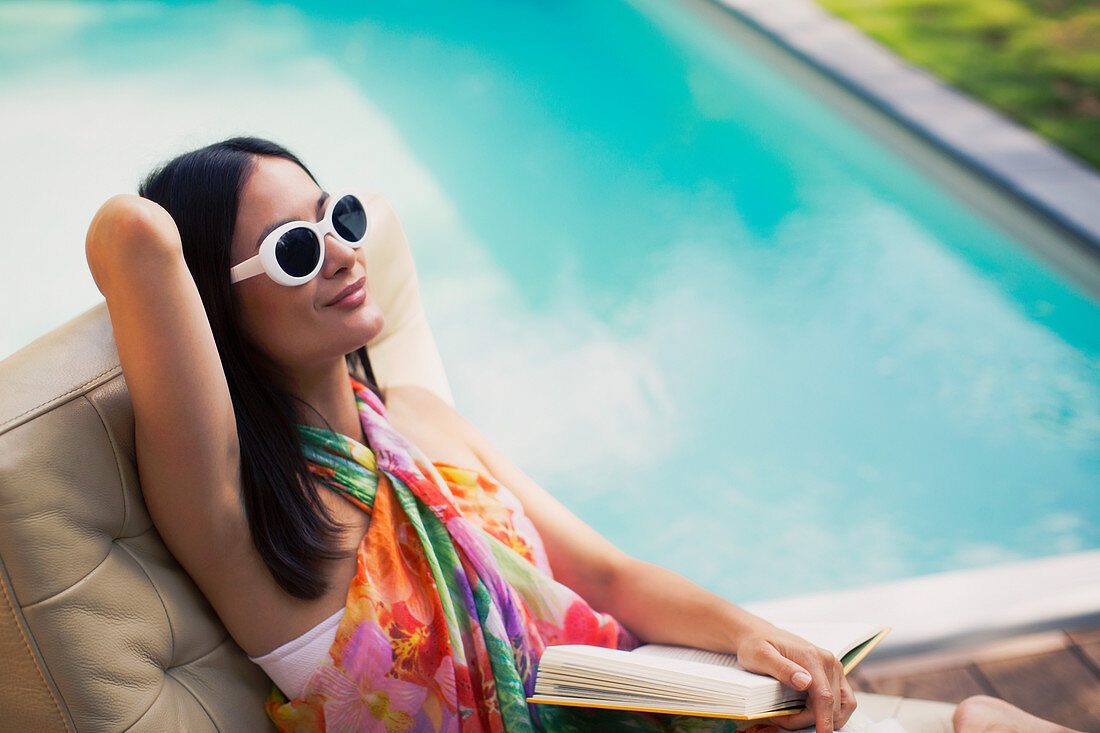 Serene woman relaxing, reading book at summer poolside