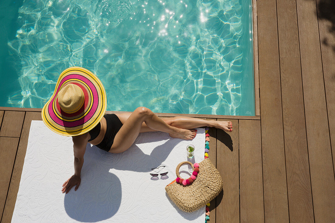 Woman in sun hat sunbathing, relaxing at summer poolside