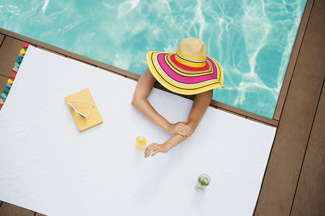 Woman in sun hat applying sunscreen in swimming pool