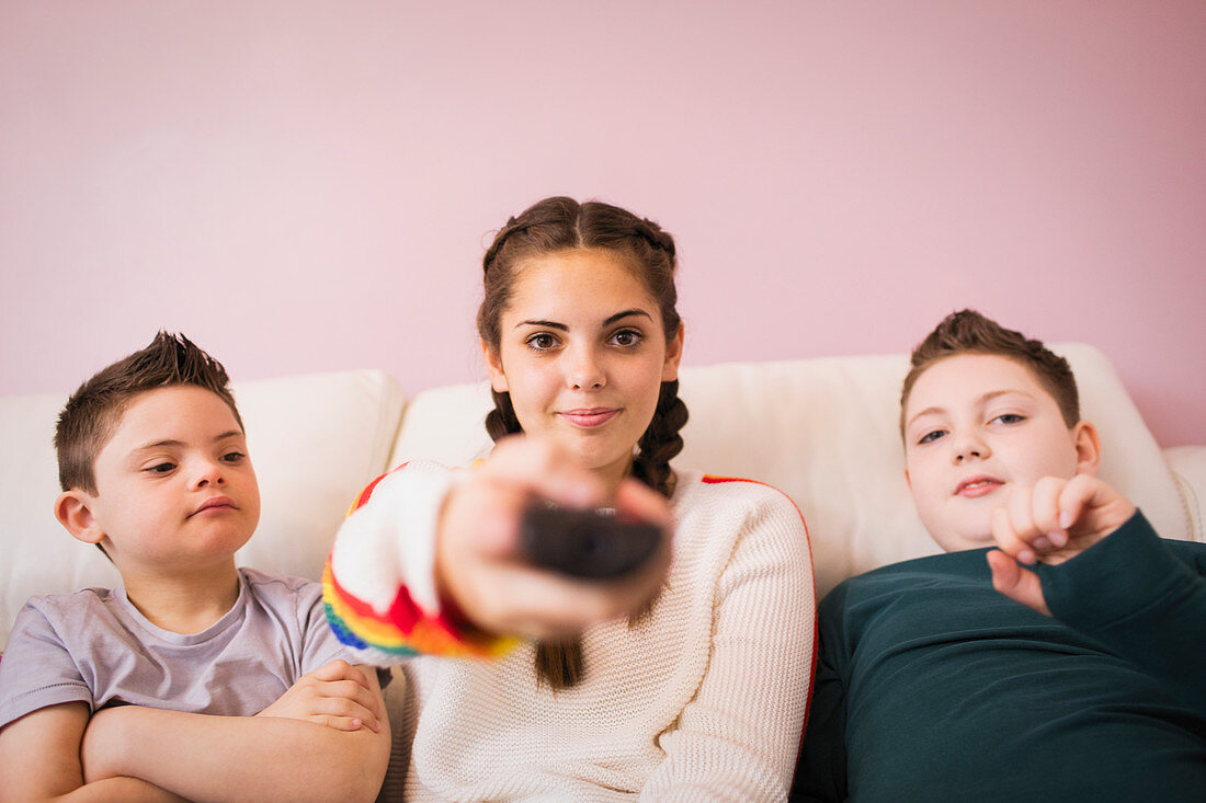 Girl with remote control watching TV with brothers