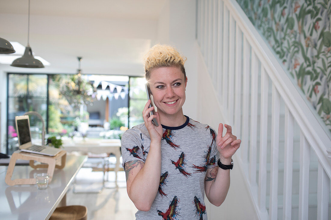 Smiling freelancer talking on smart phone in kitchen