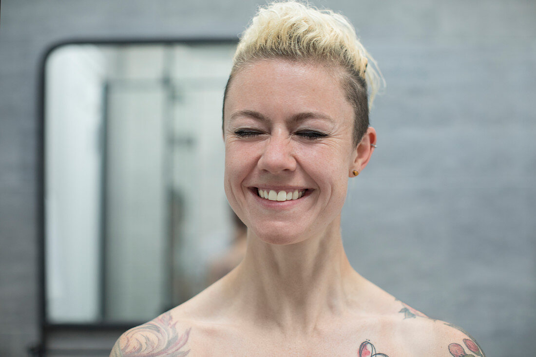 Carefree woman with tattoos laughing in bathroom