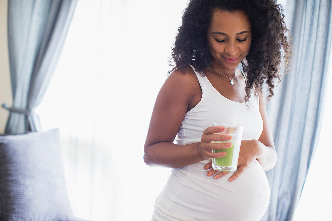 Young pregnant woman drinking green smoothie