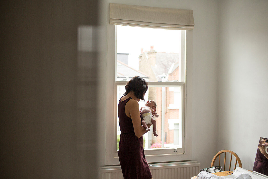 Mother holding innocent newborn baby boy at window