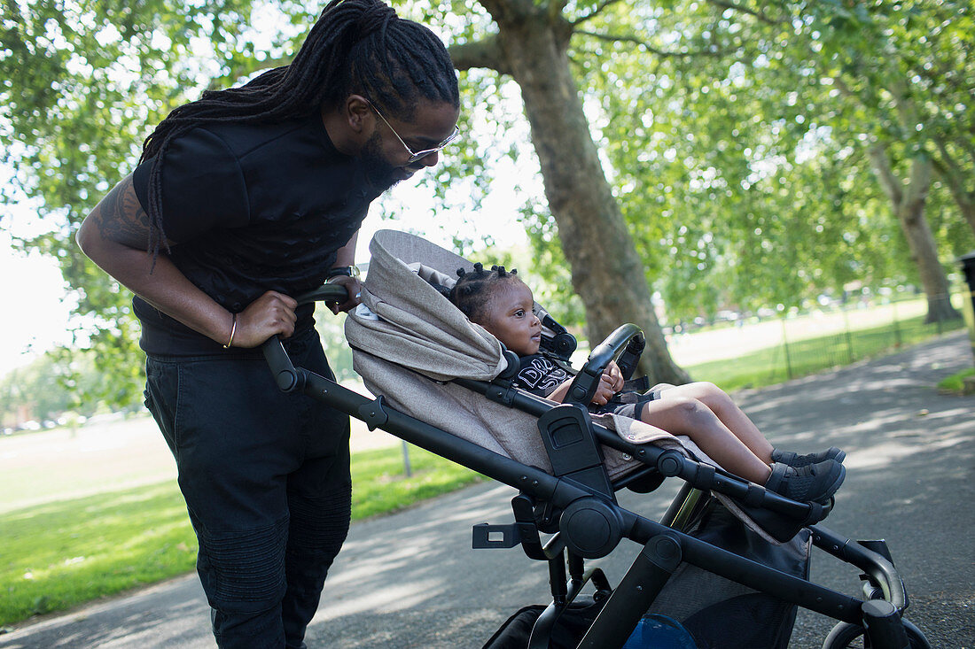 Father pushing toddler son in stroller in park