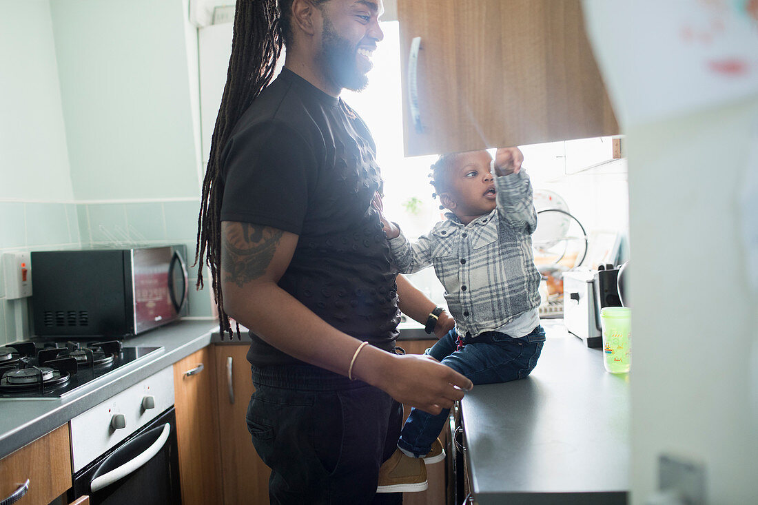 Father and toddler son opening cupboard in kitchen