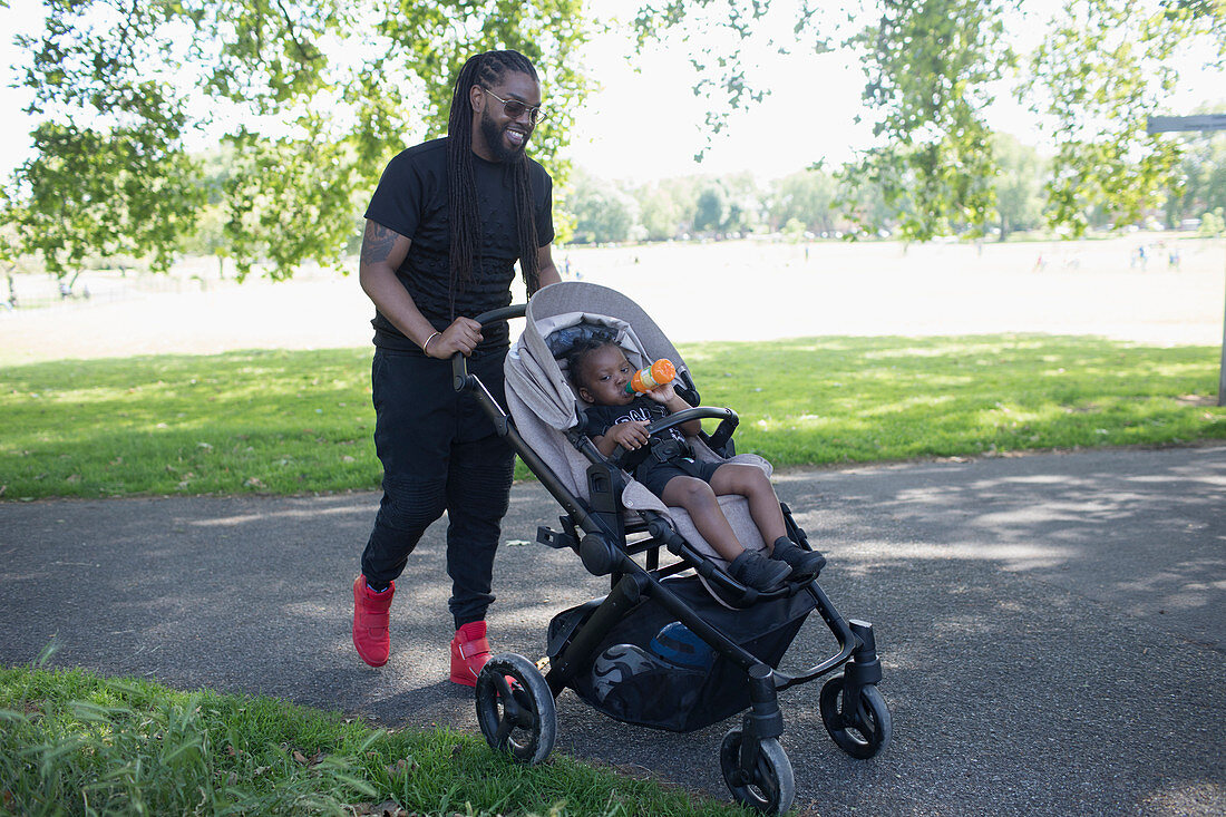 Father pushing toddler son in stroller in park