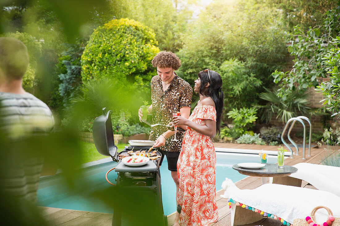 Young multiethnic couple barbecuing at summer poolside