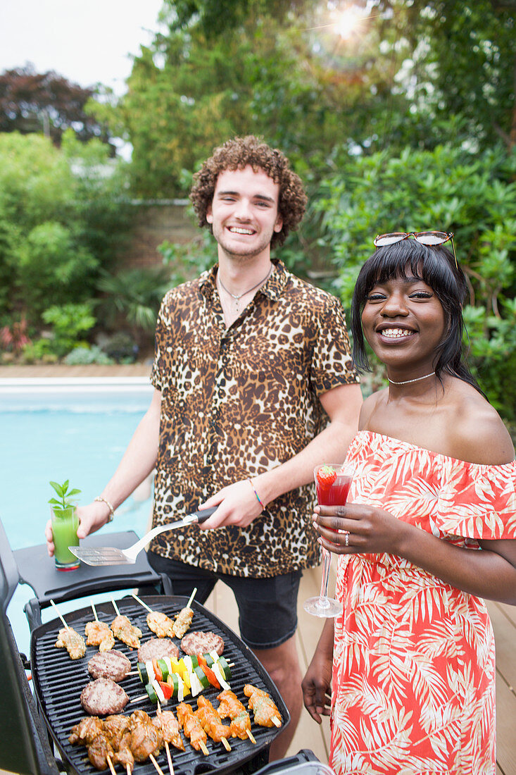 Portrait happy multiethnic couple barbecuing at poolside