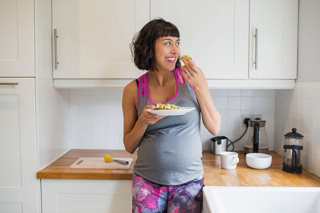 Happy pregnant woman eating in kitchen