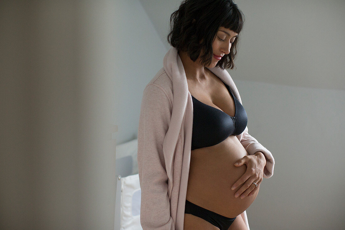 Serene pregnant woman in bra and panties rubbing stomach