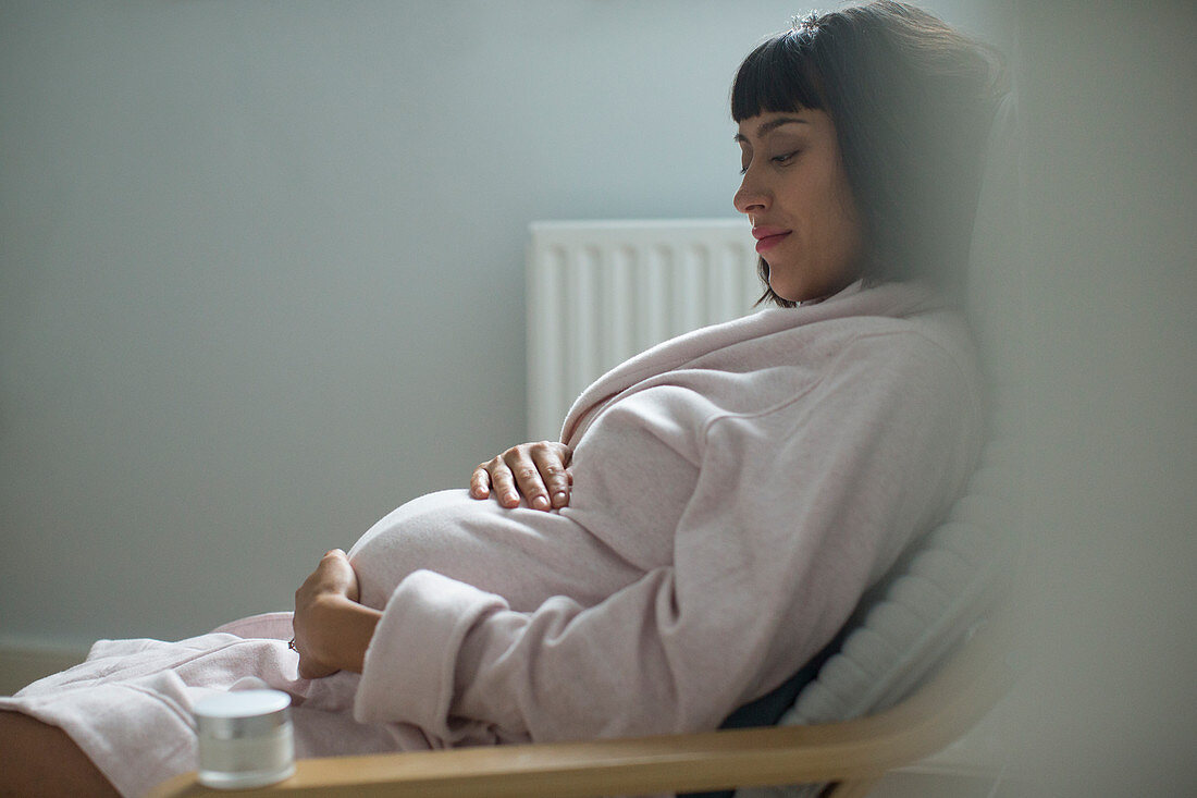 Serene pregnant woman in bathrobe holding stomach