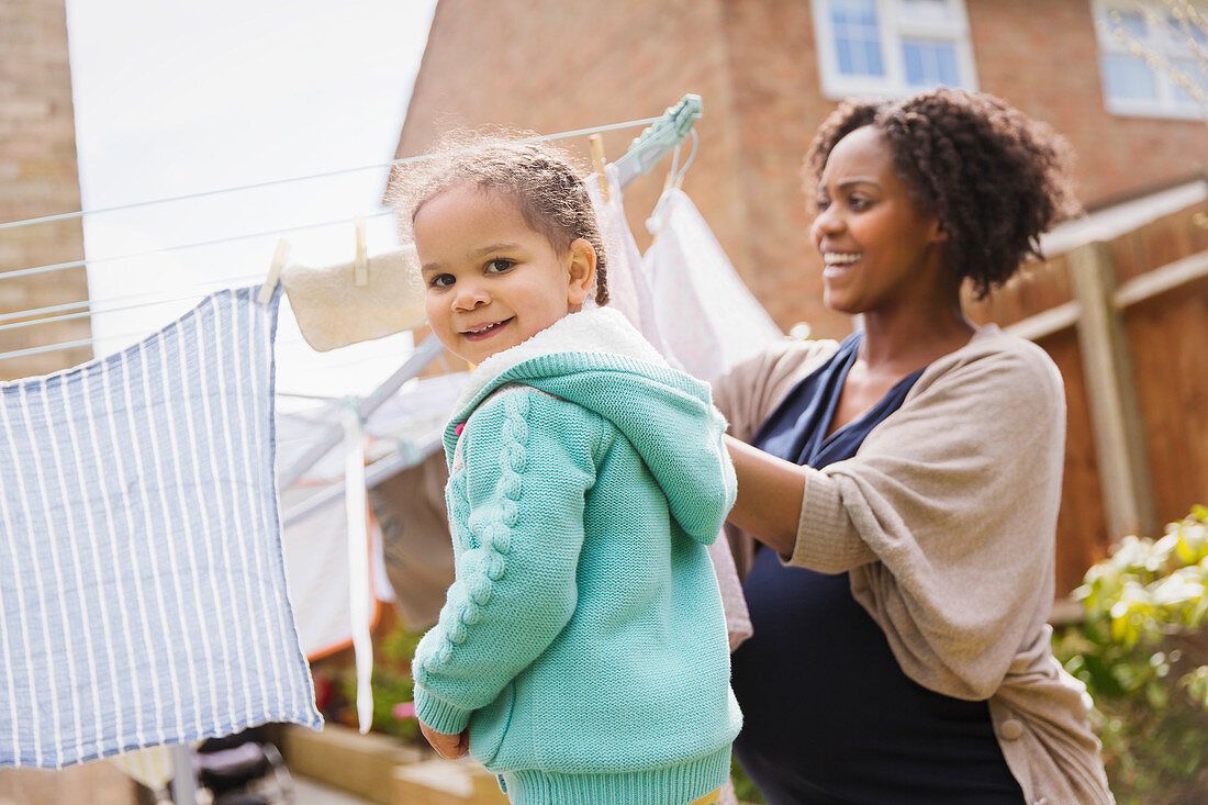 Girl helping pregnant mother hang laundry on clothesline