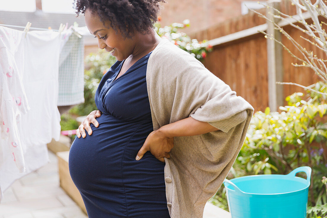 Happy pregnant woman hanging laundry on clothesline