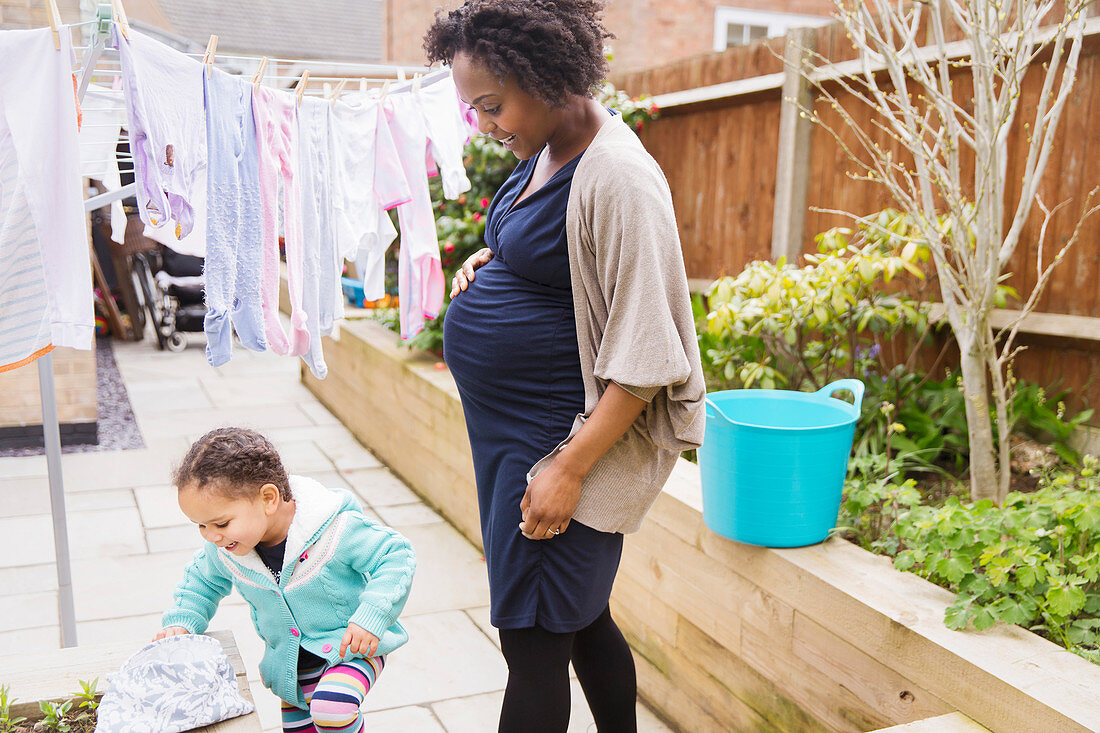 Pregnant mother and daughter hanging laundry