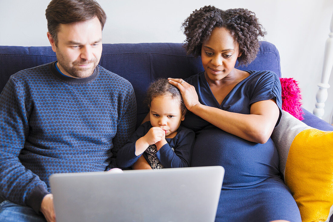 Pregnant family using laptop on sofa