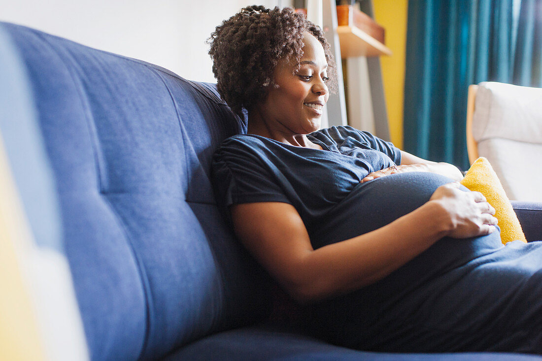 Happy pregnant woman touching stomach on sofa