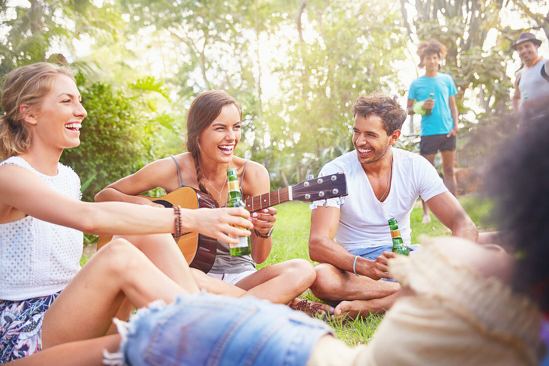 Friends hanging out drinking and playing guitar in park