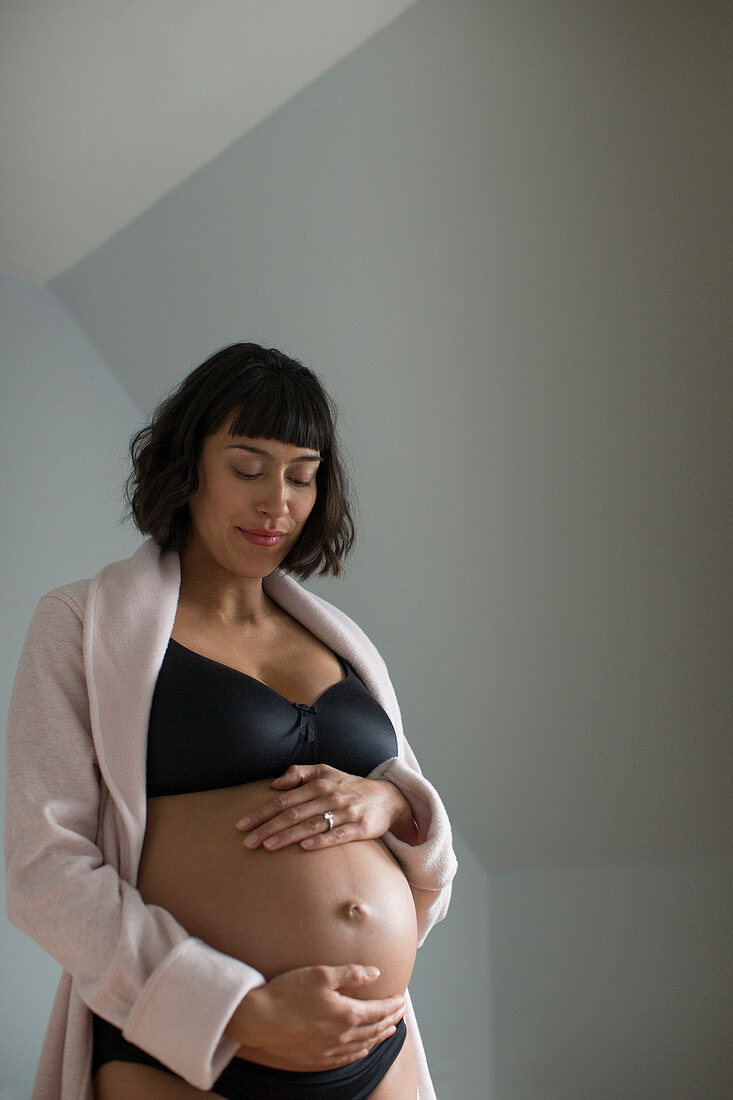 Pregnant woman in bra holding stomach