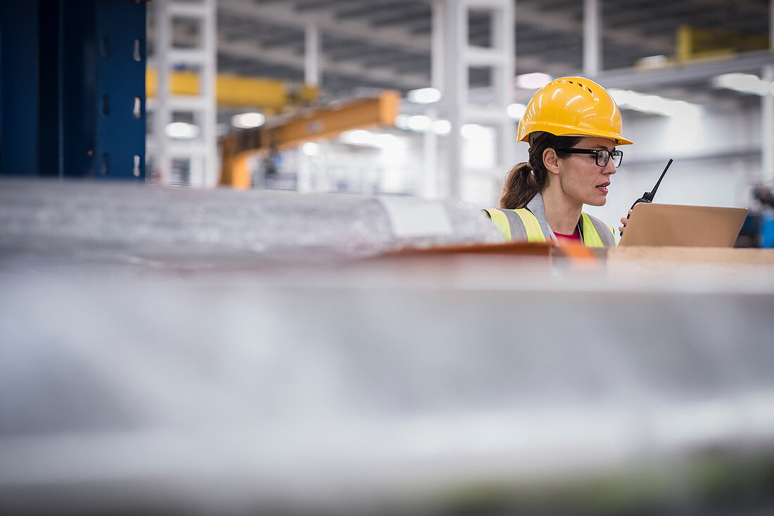 Female worker using laptop and walkie-talkie in factory