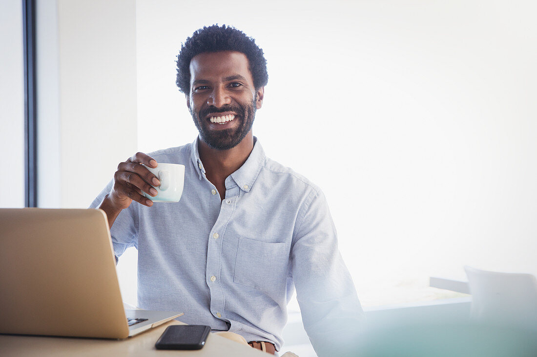 Smiling, confident businessman drinking coffee at laptop