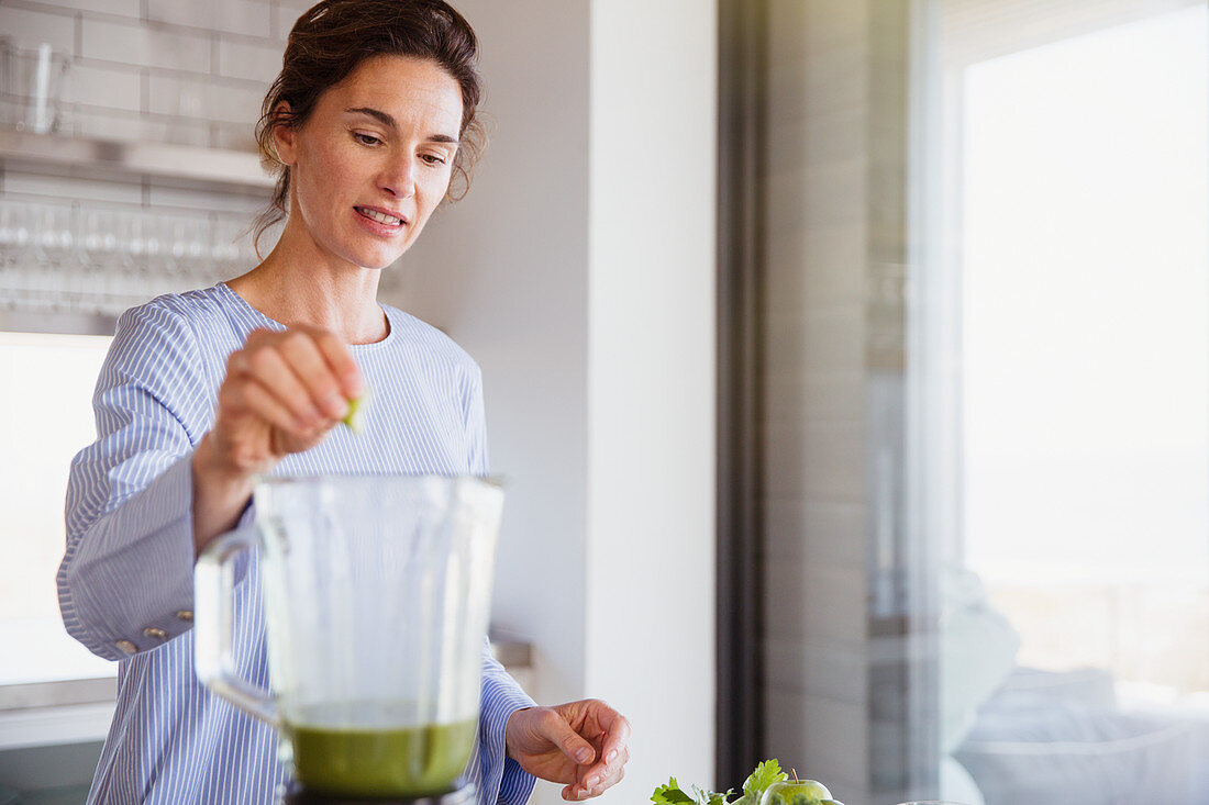 Woman making healthy green smoothie in blender in kitchen