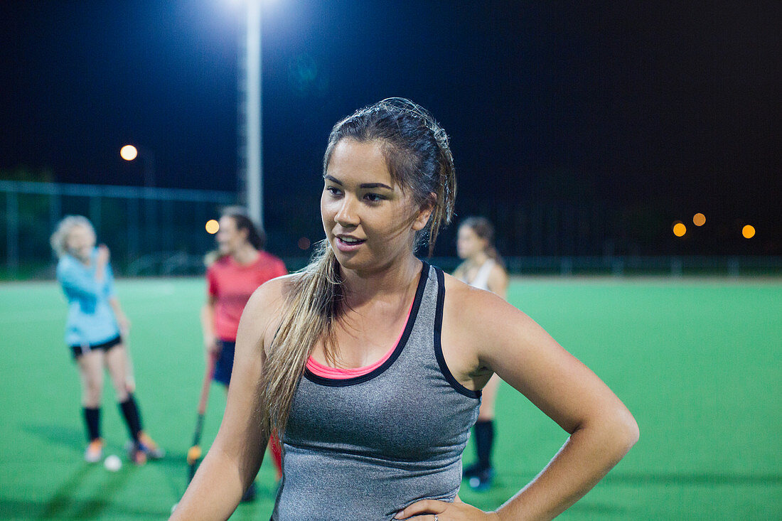 Tired young female hockey player resting on field at night