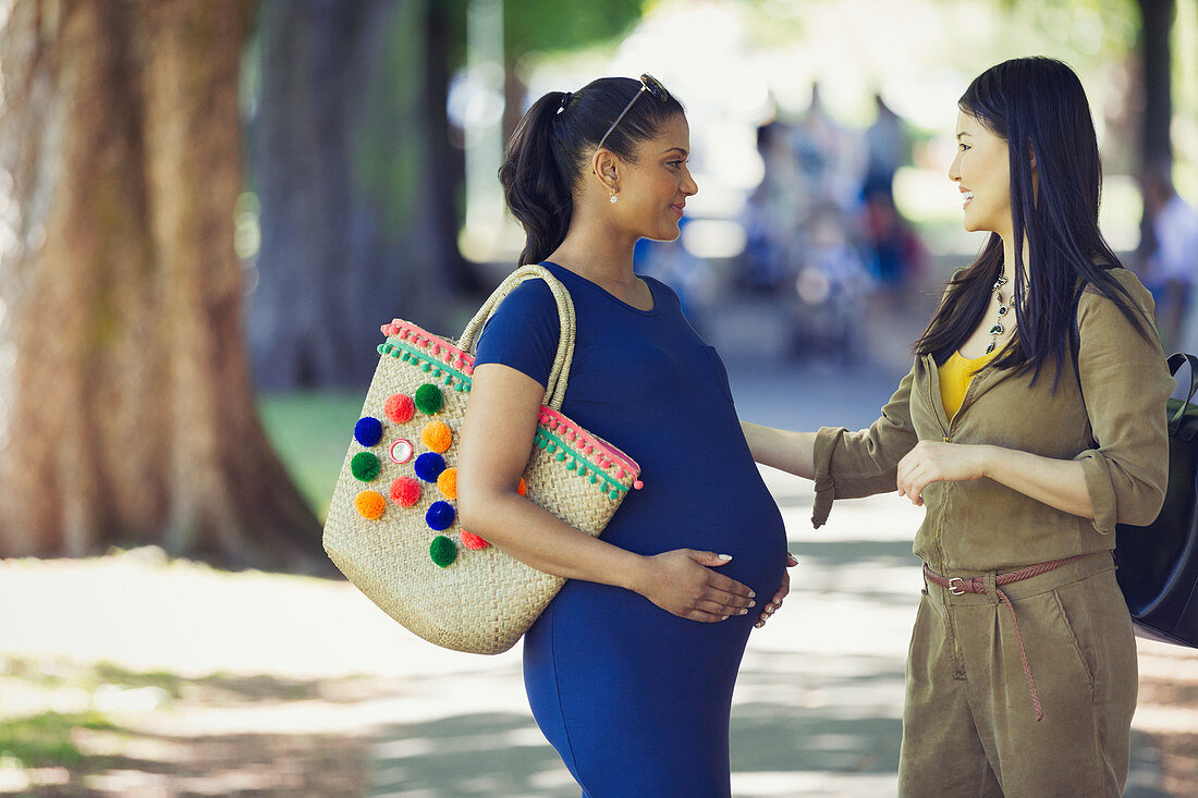 Woman greeting pregnant friend in park