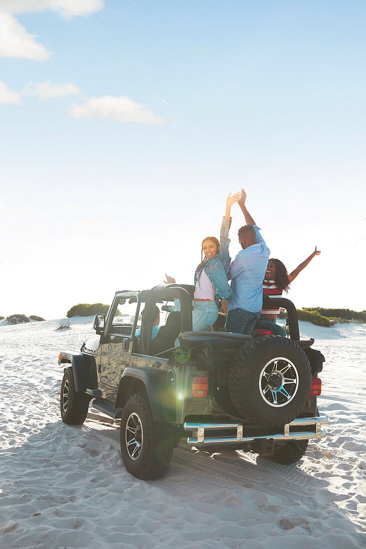 Friends cheering with arms raised in jeep on beach