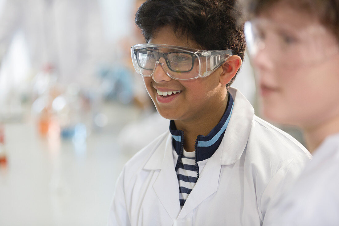 Smiling boy wearing goggles and lab coat in classroom