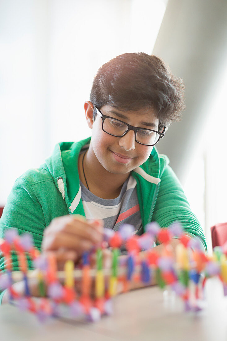 Smiling boy student assembling DNA model in classroom
