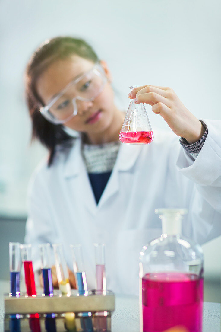 Girl student examining pink liquid in laboratory classroom