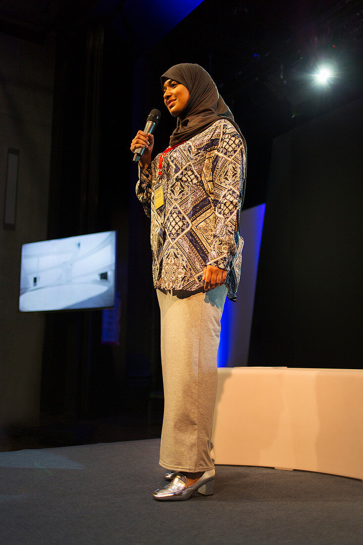 Female speaker in hijab talking with microphone on stage