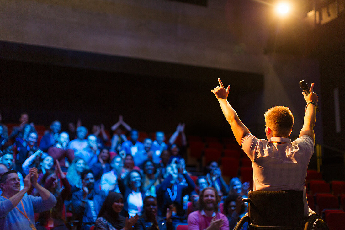 Speaker in wheelchair on stage cheering with audience