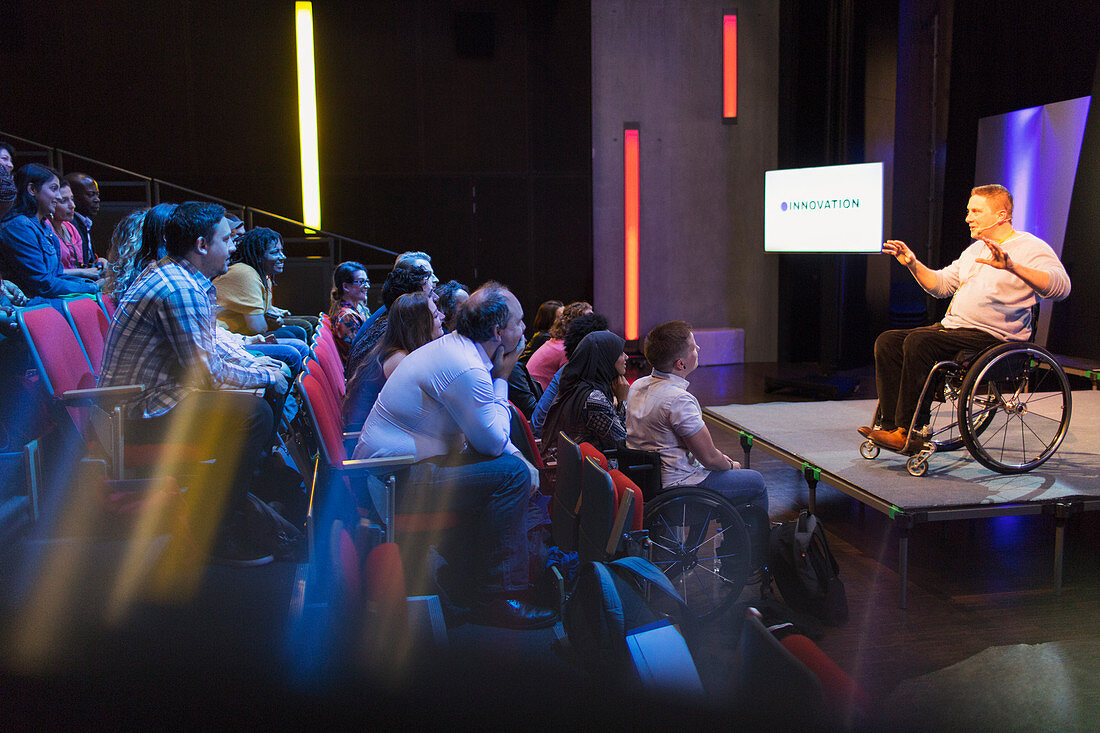 Audience listening to female speaker in wheelchair on stage