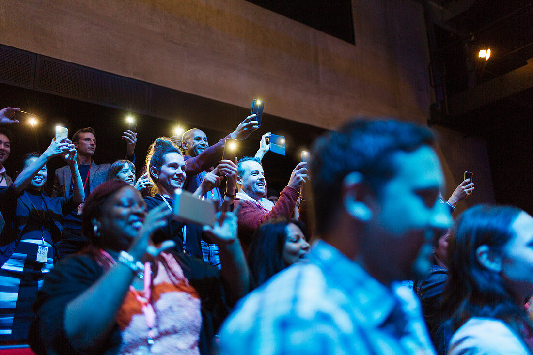 Enthusiastic audience with camera phones in dark auditorium