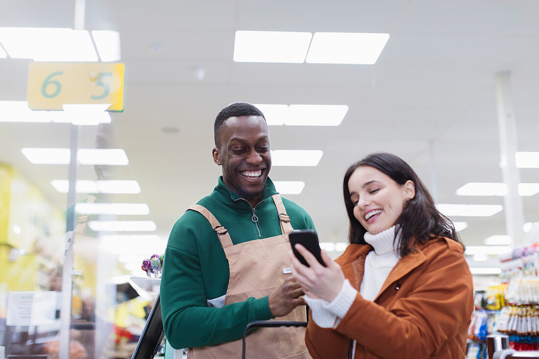 Grocer helping customer with smart phone in supermarket