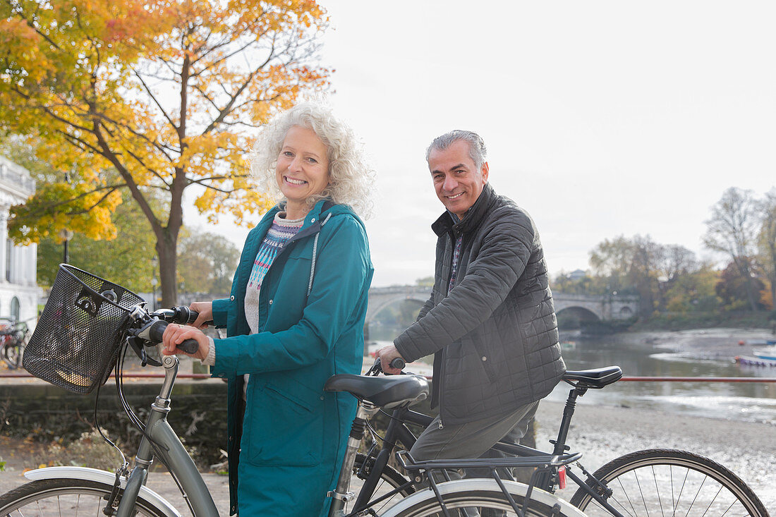 Smiling senior couple bike riding along autumn river