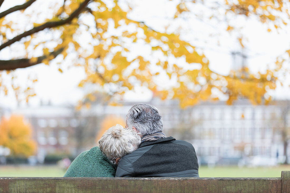 Affectionate senior couple cuddling on bench in autumn park