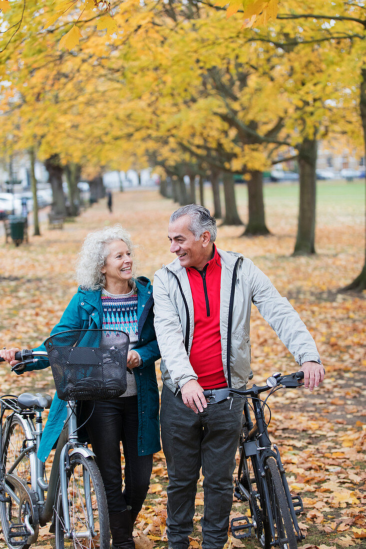 Senior couple walking bicycles among trees in autumn