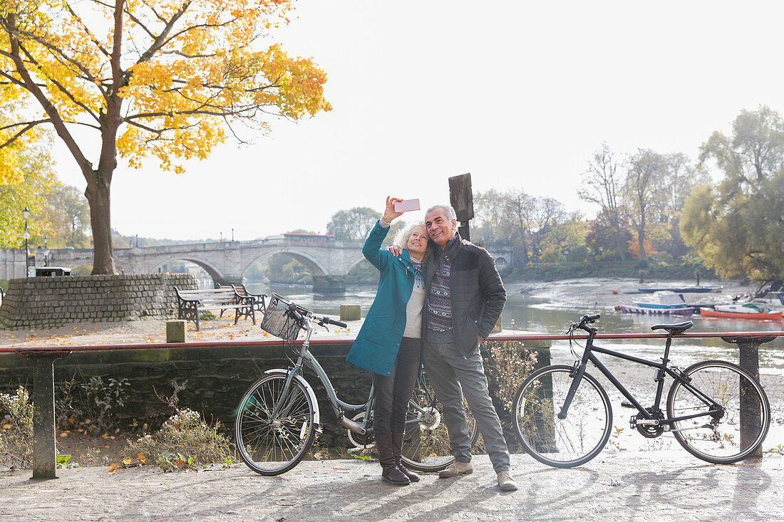 Senior couple with bicycles taking selfie at autumn river