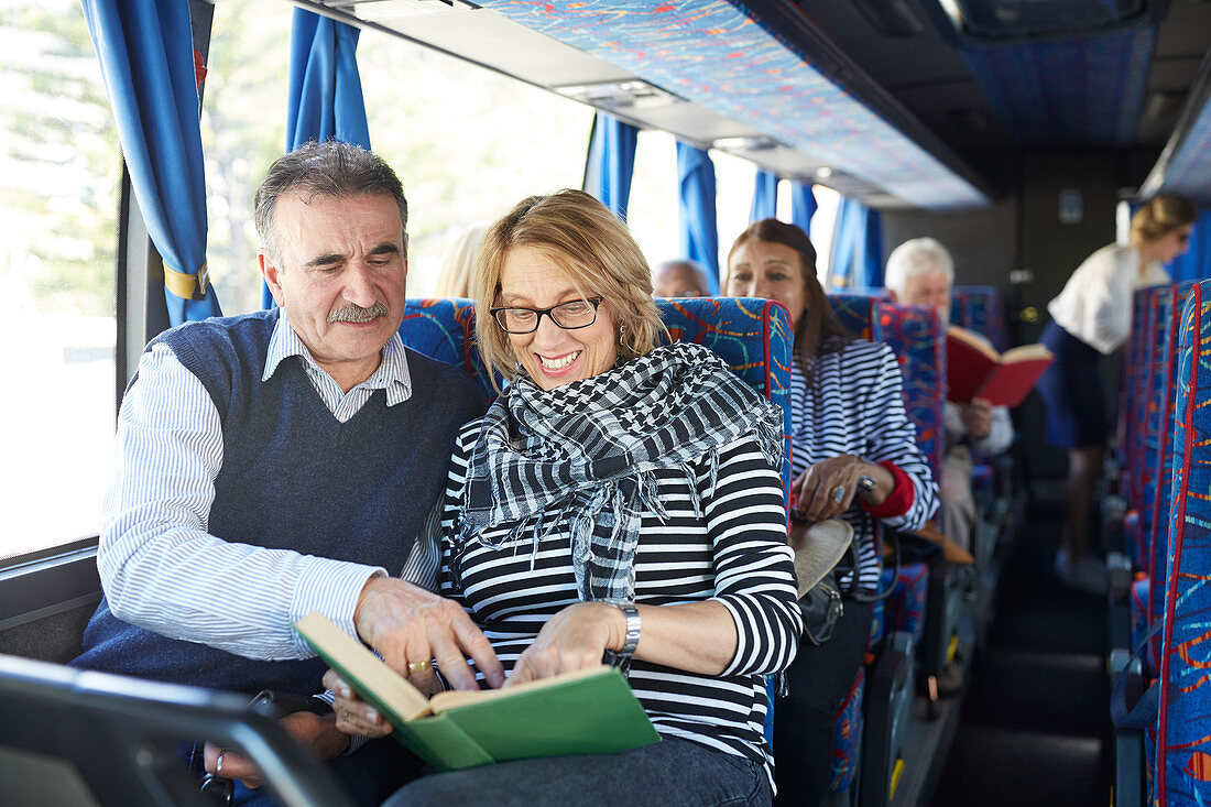 Active senior couple tourist reading book on tour bus