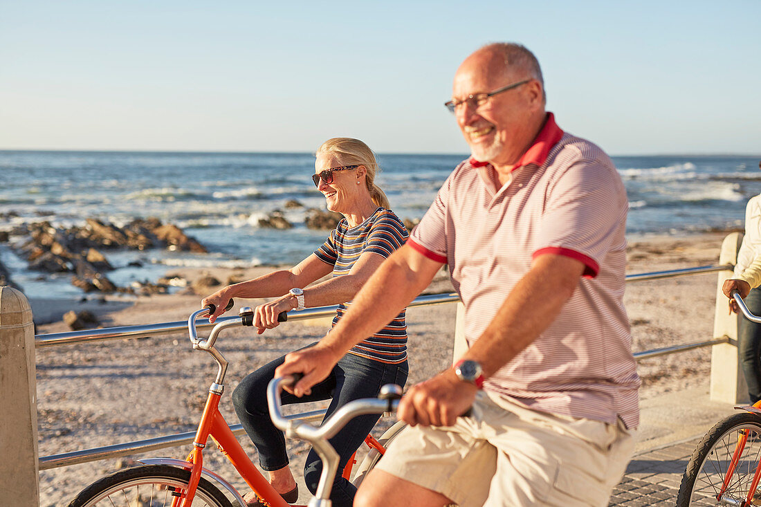 Smiling active senior tourists bike riding along sunny ocean