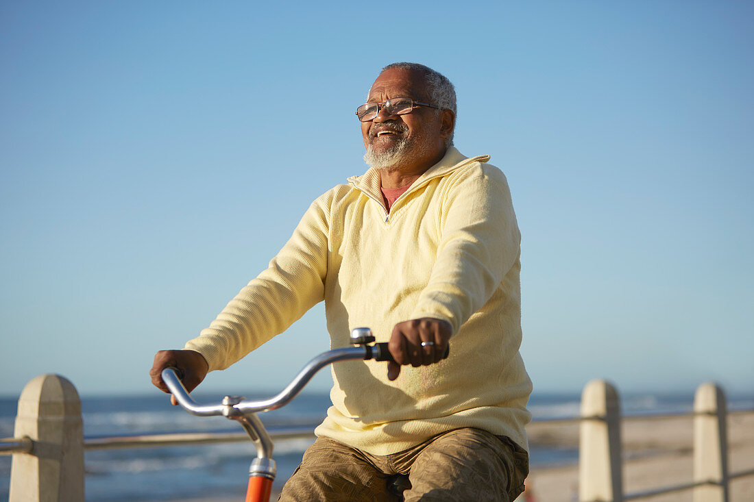Carefree active senior man tourist bike riding along ocean