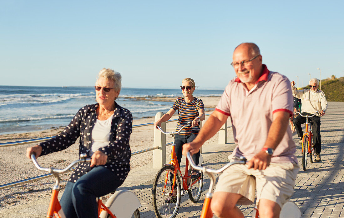 Active senior tourist friends bike riding along ocean