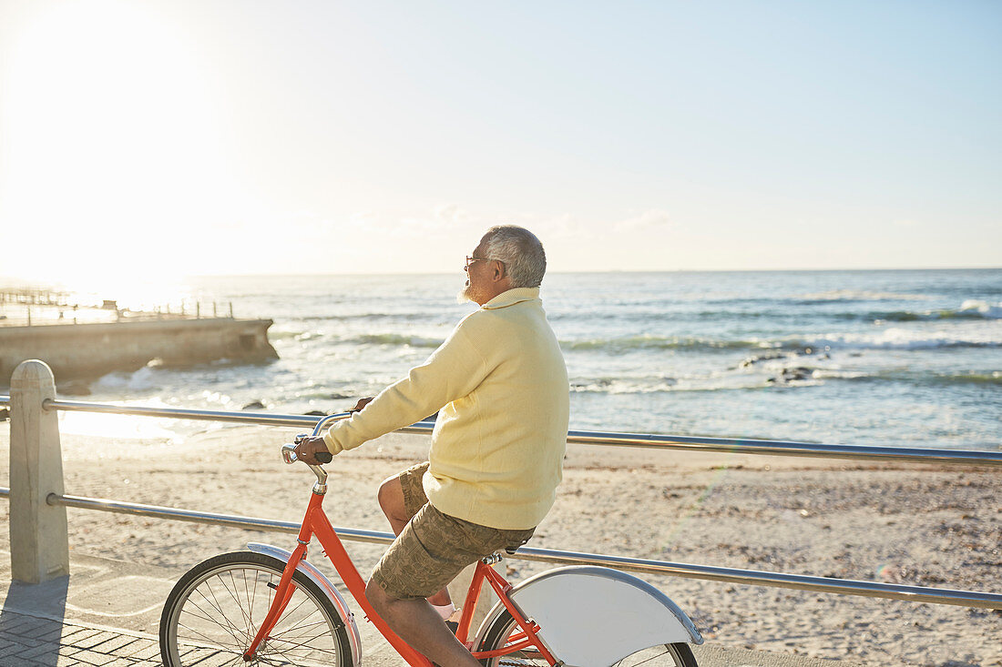 Senior man tourist bike riding on boardwalk along ocean