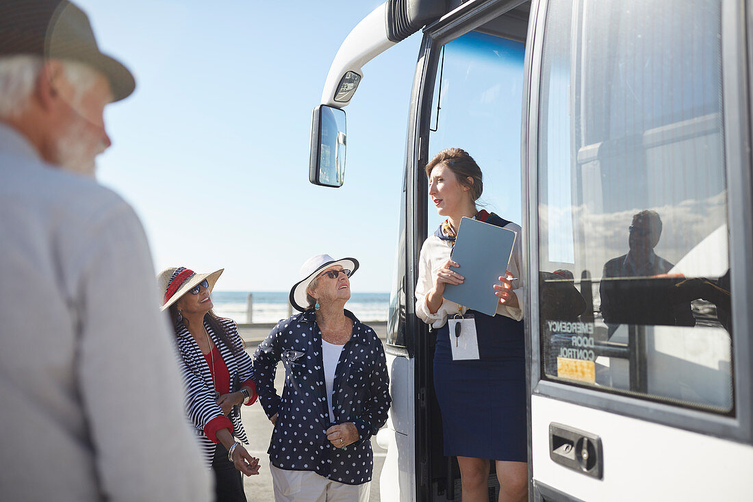 Tour guide talking to senior tourists at doorway of tour bus